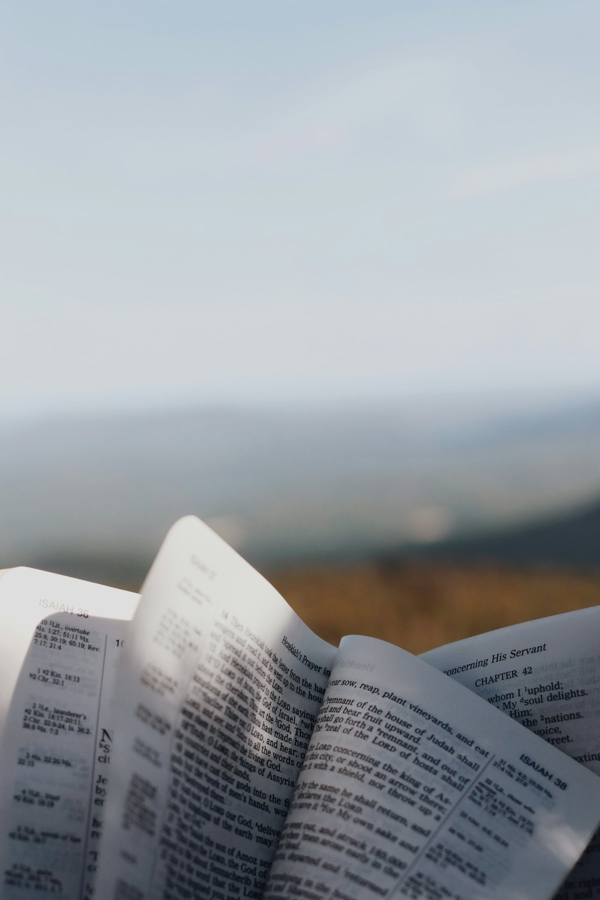 An open Bible held up against hills and sky